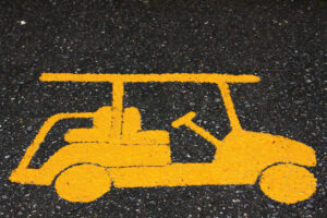 A yellow golf cart road sign on pavement