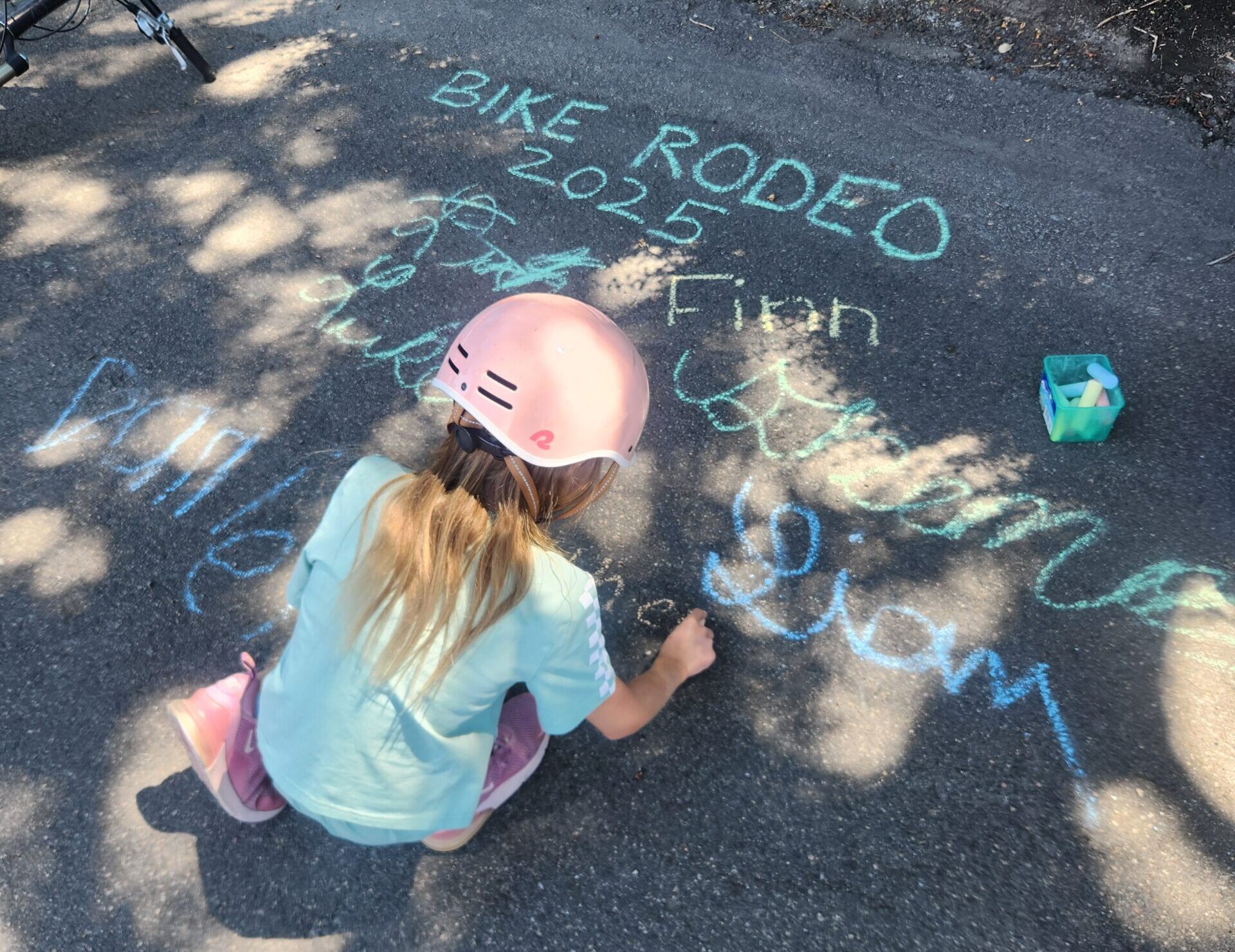 young girl making a sidewalk chalk sign for bike rodeo 2025